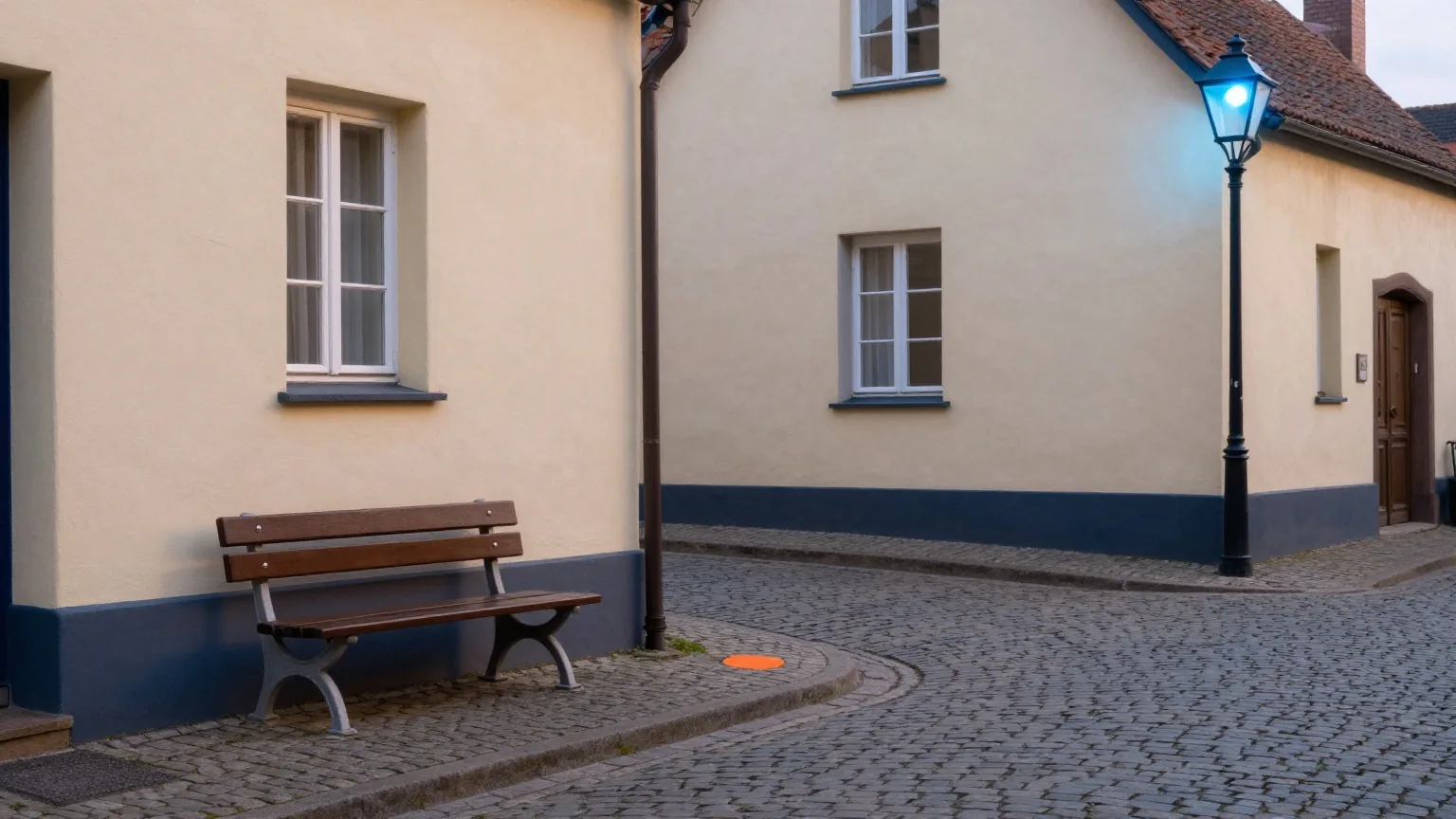 Leere Kopfsteinpflastergasse in der Altstadt in der Morgendämmerung mit Holzbank und noch brennender Straßenlaterne