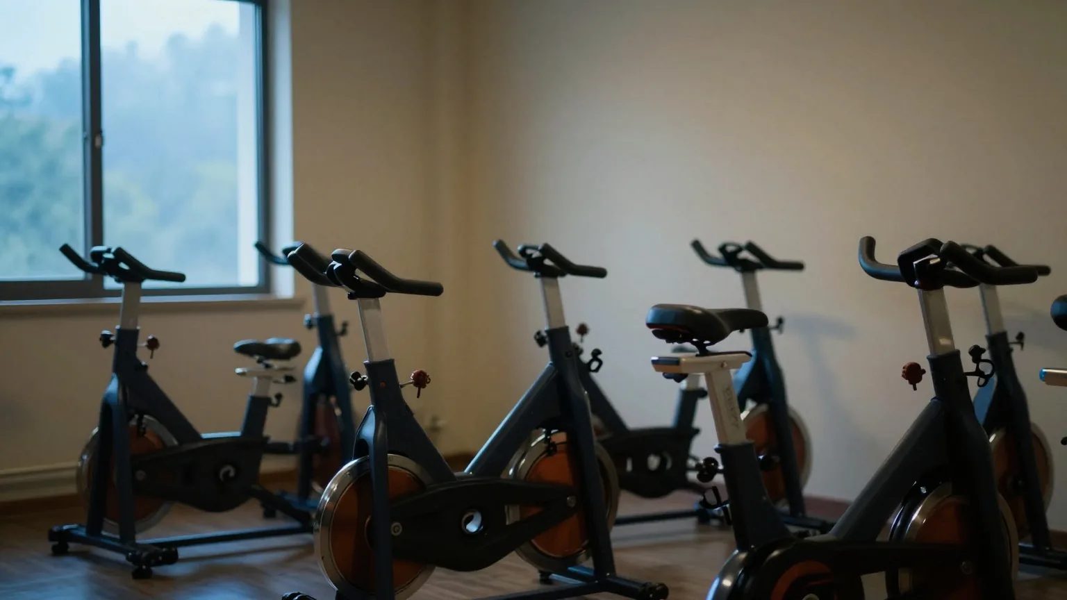 Reihe leerer Indoor-Cycling-Räder in einem gedämpft beleuchteten Kursraum, weiches blaues Licht fällt am frühen Morgen durch ein seitliches Fenster