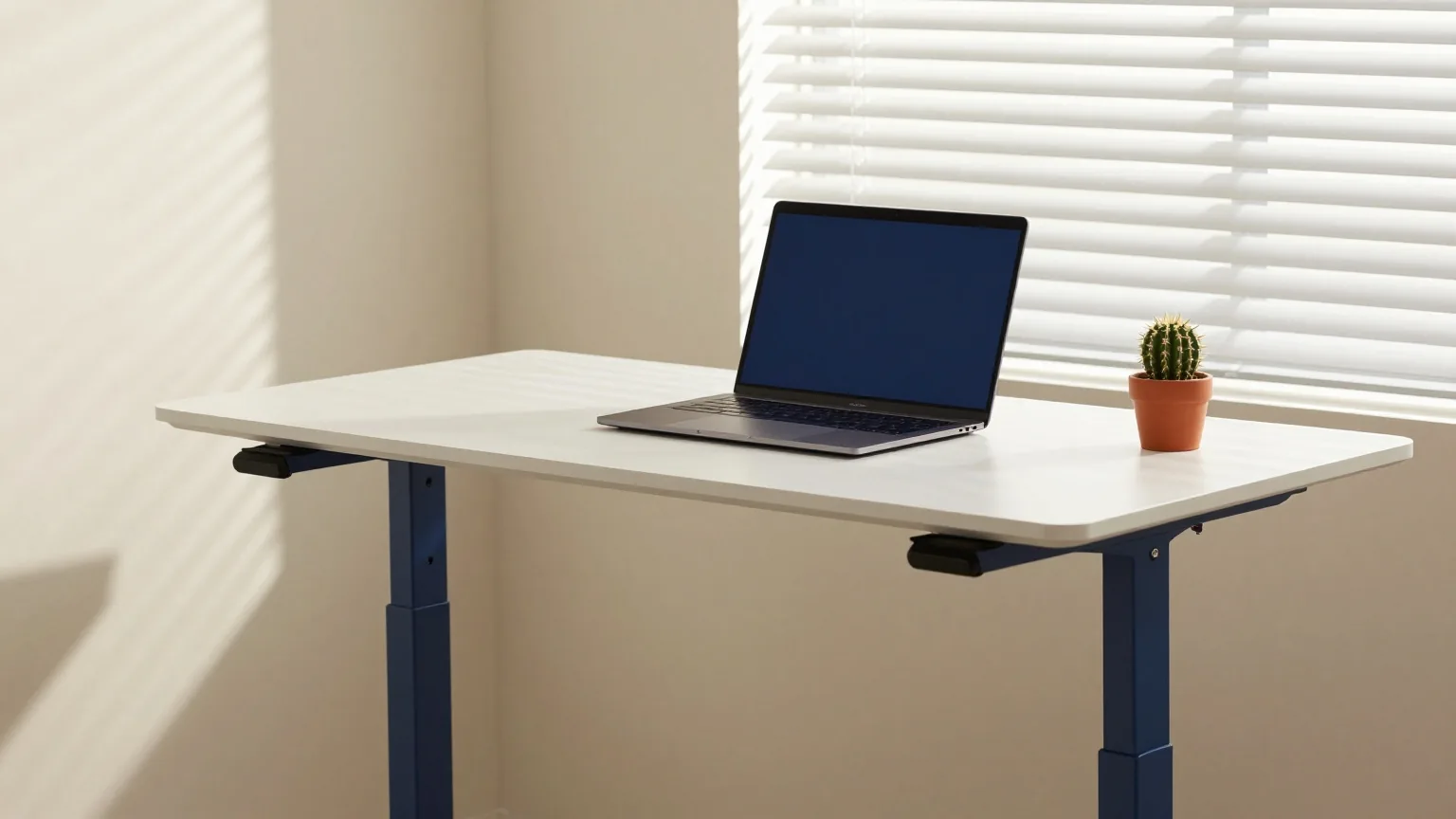 Stehschreibtisch in einem schlichten Arbeitszimmer mit zugeklapptem Laptop und kleinem Kaktus, kühles Morgenlicht durch Jalousien