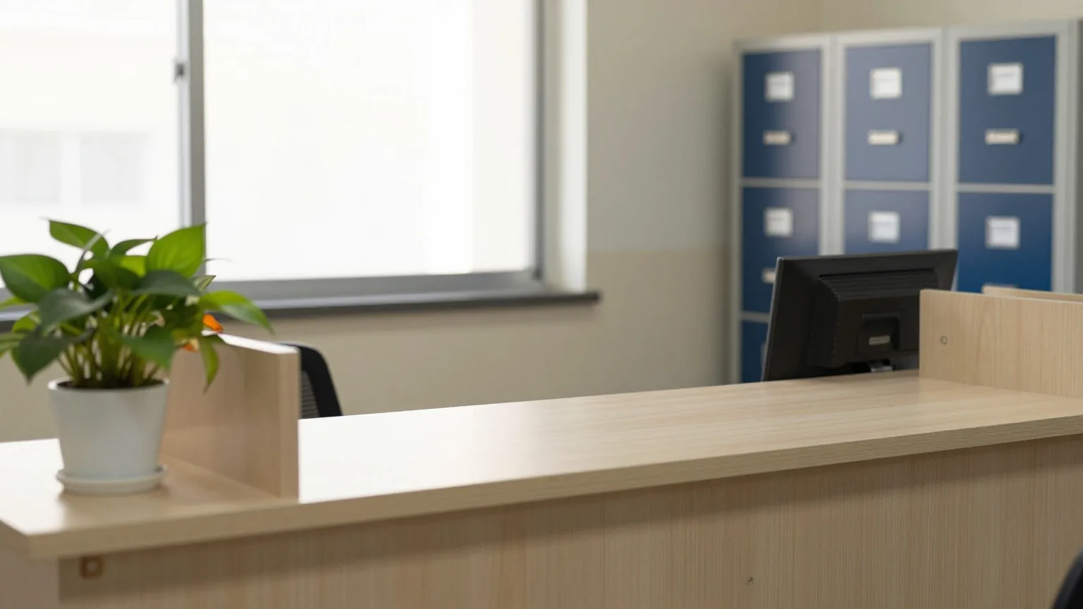 Leerer Kundenschalter in einem kleinen Stadtwerke-Büro am Morgen mit hellem Holztresen, Zimmerpflanze und grauen Schränken