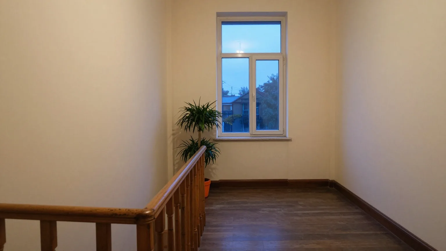 Leerer Treppenabsatz in einem Altbau in der Abenddämmerung mit Holzgeländer und einer Topfpflanze am hohen Fenster