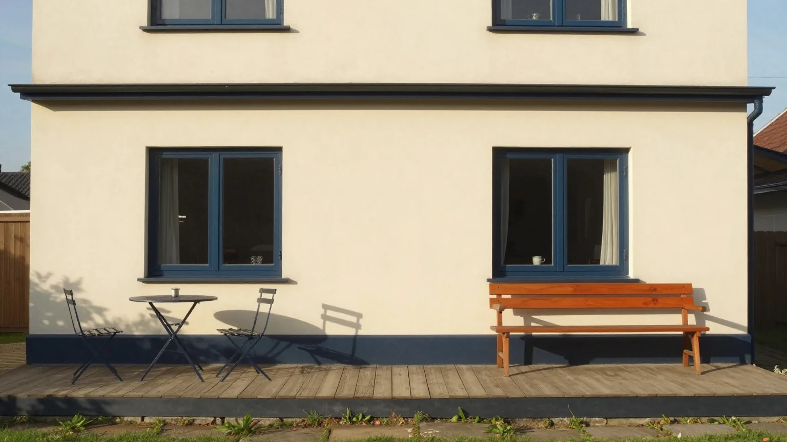Garten hinter einem zweigeschossigen Haus mit zwei getrennten Terrassen, auf der einen ein Bistrotisch, auf der anderen eine Holzbank